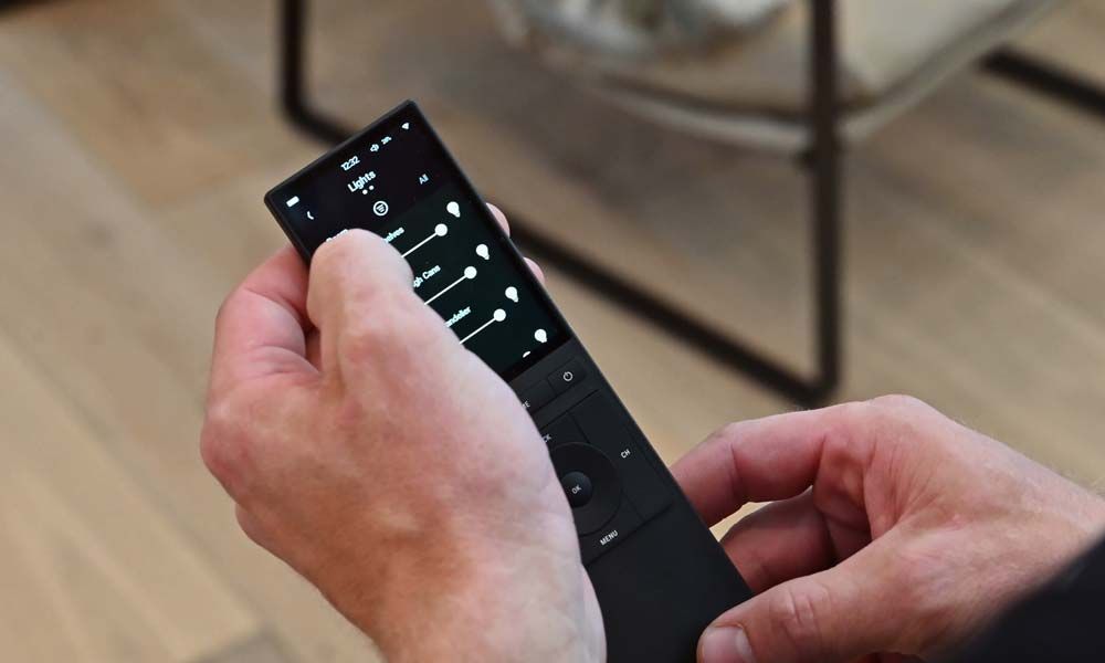 A close-up of hands adjusting light settings using a sleek remote control in a modern room.