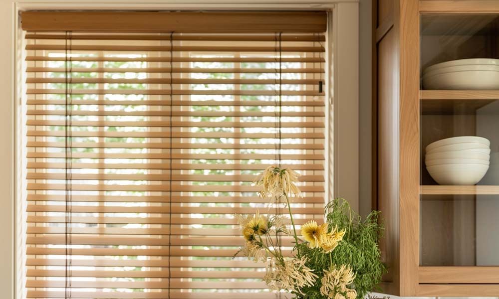 Light wooden blinds in a kitchen with natural light and fresh flowers on the countertop.