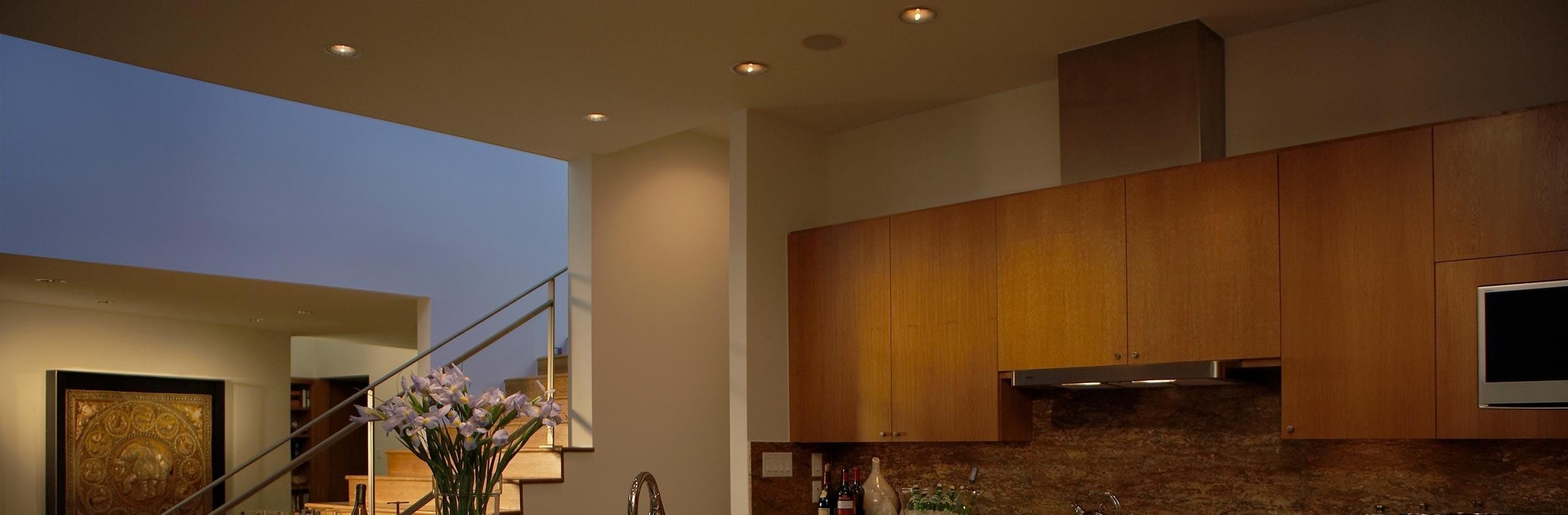 Cozy kitchen with wooden cabinets, recessed ceiling lights, and a staircase in the background.