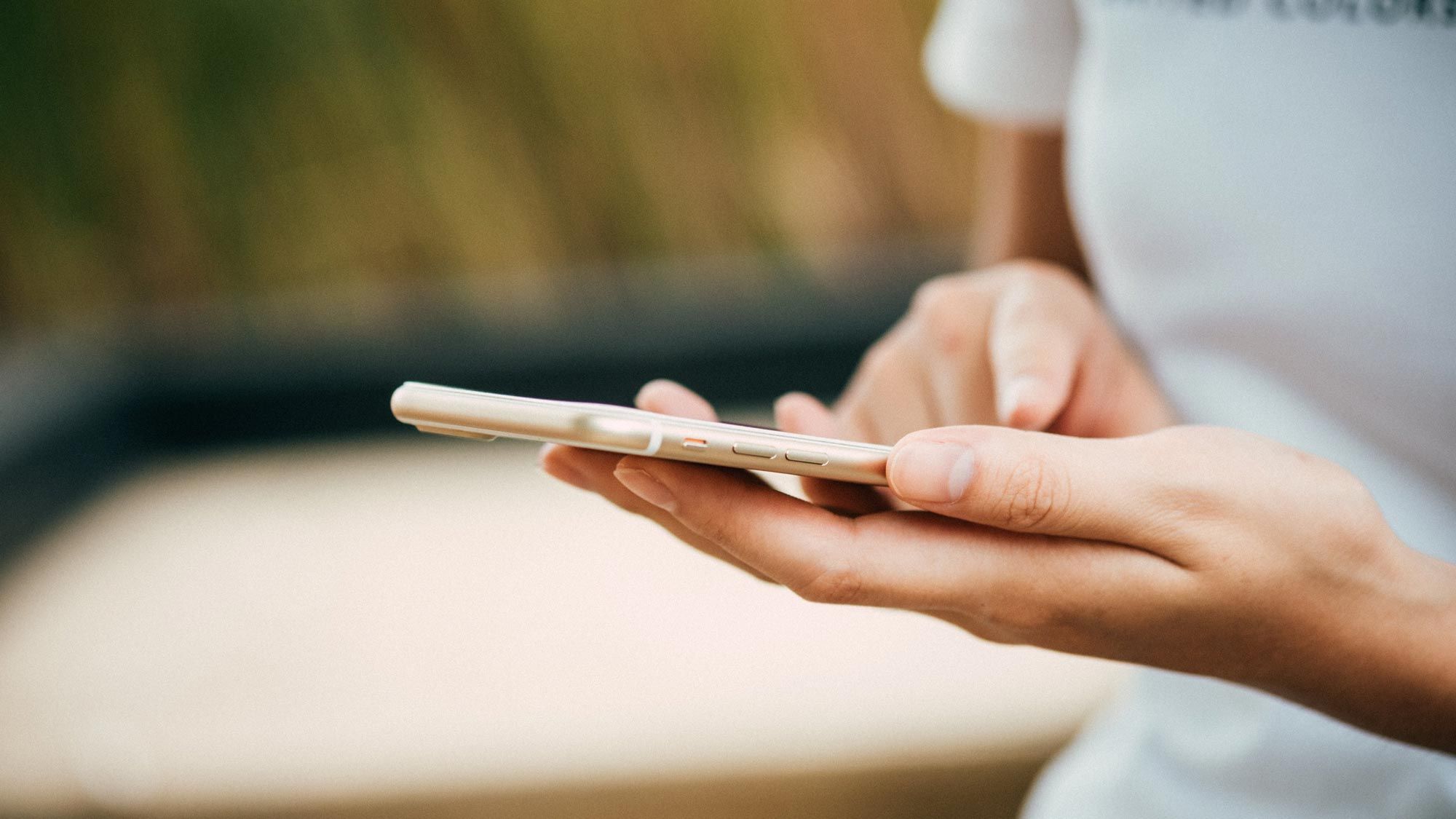 A close-up of hands holding a smartphone outdoors, controlling smart home features.