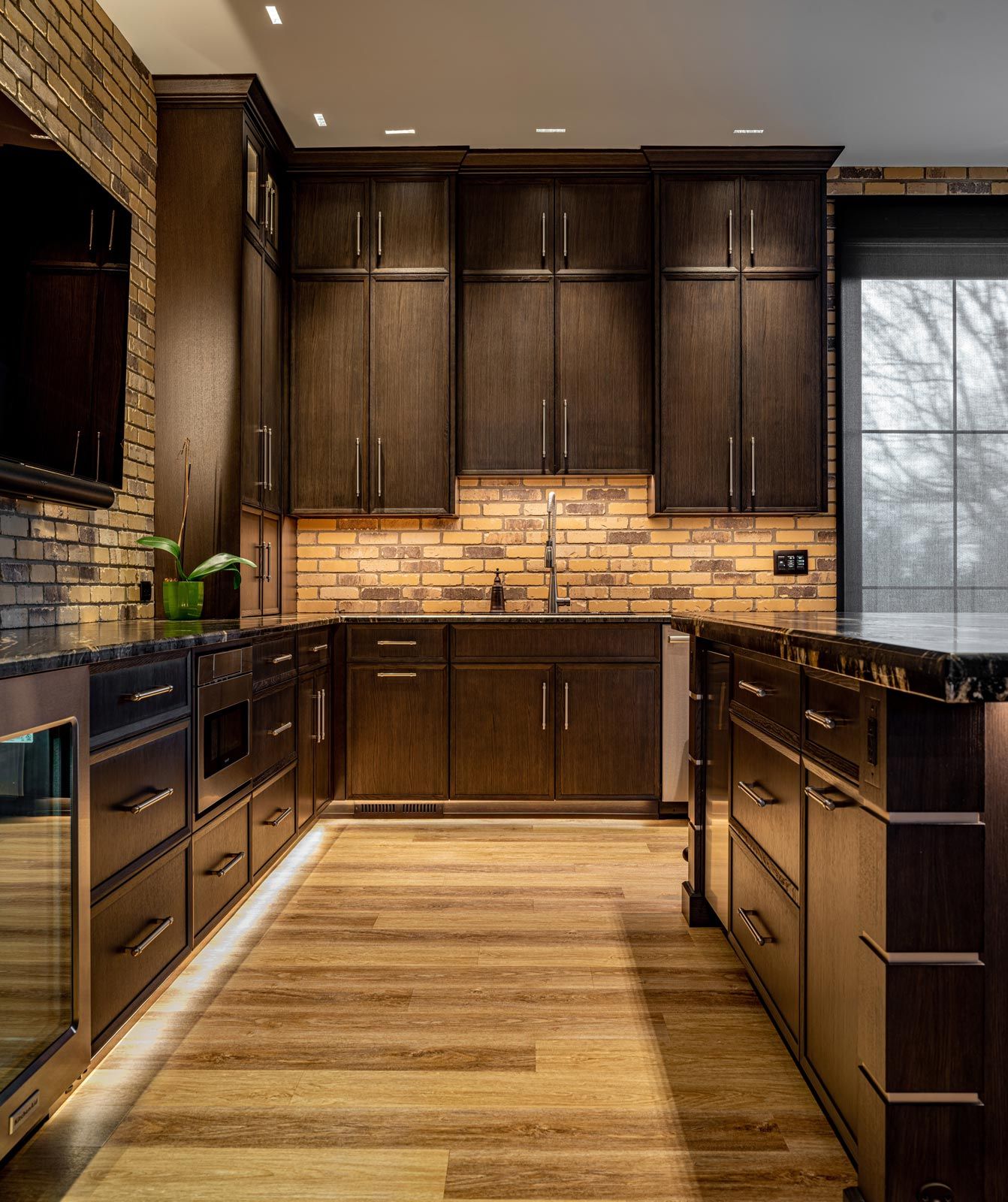 Traditional kitchen in wood and chocolate tones and a TV hanging in an accent brick wall.