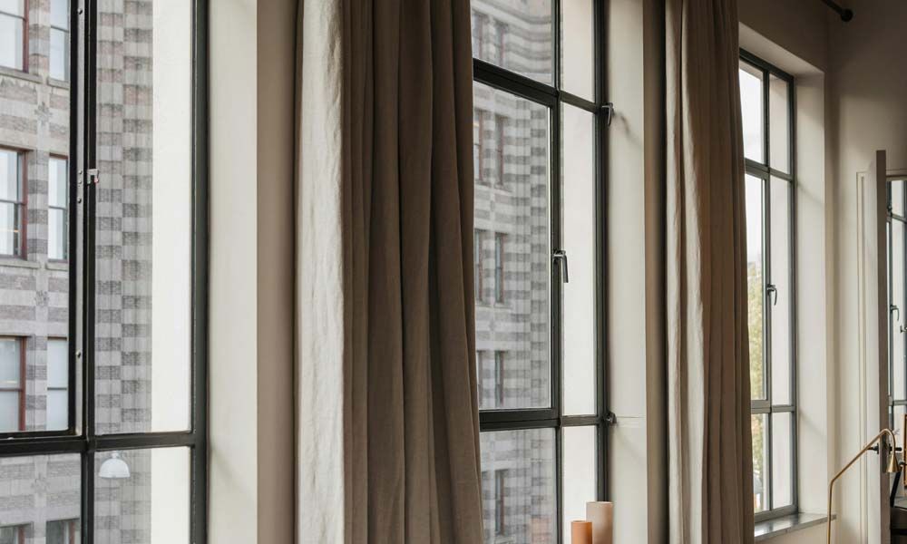 Large industrial-style windows with neutral-colored curtains, offering a balance of light and privacy.