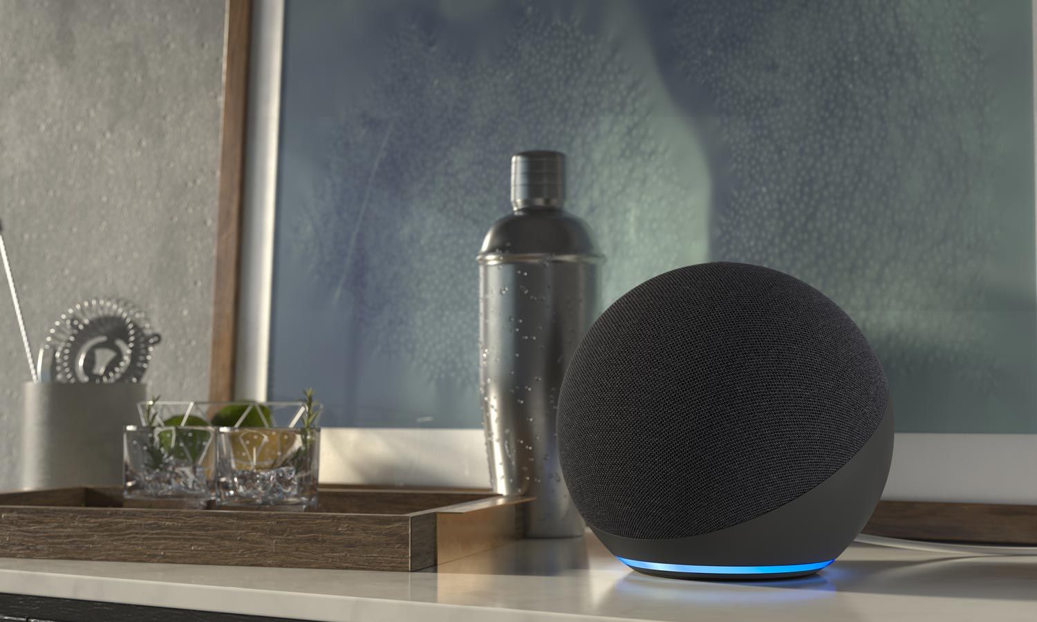 A modern smart speaker with a glowing base on a countertop next to a tray with cocktail ingredients.